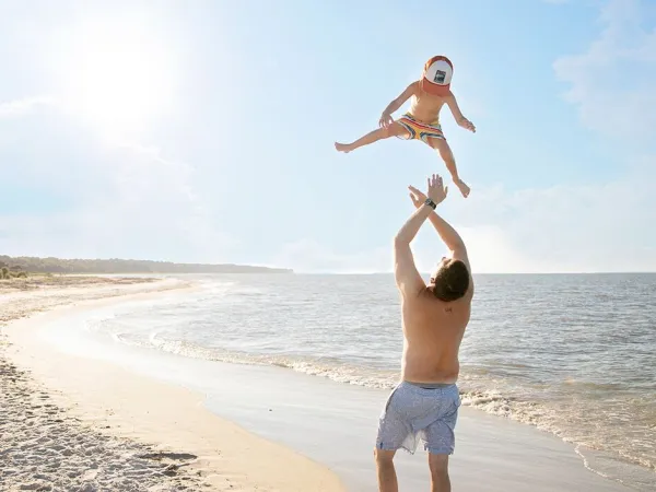Father throws little boy into the air on the beach at Roan camping Sole Family Camping Village.