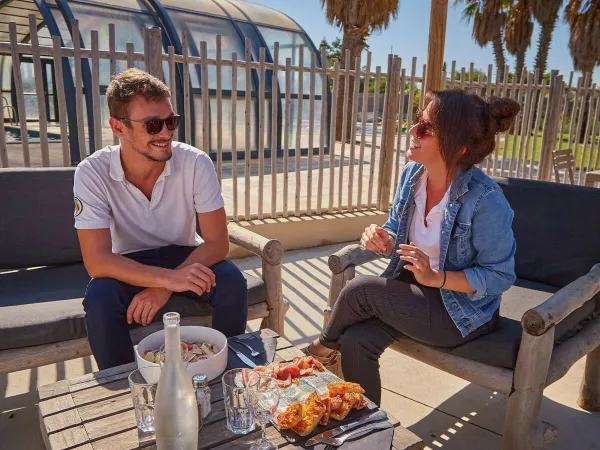 2 people having drinks on the terrace at Roan camping Les Dunes.