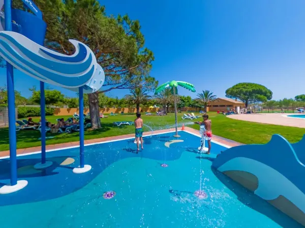 Spray park and sunbathing area with sunbeds in the shade at Roan camping Platja Brava.