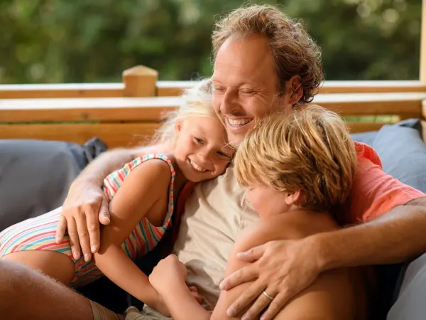 Father and children enjoying themselves on the lounge sofa of the mobile home at Roan campsite Le Petit Mousse.
