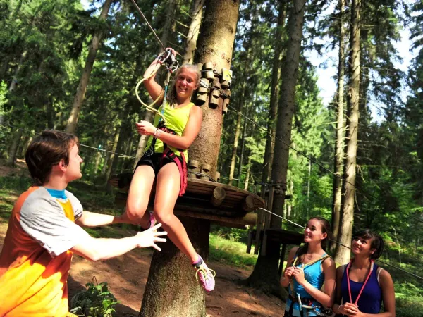 Girl swinging on the cable car at the tree climbing course at Roan campsite Le Lac des Vieilles Forges.